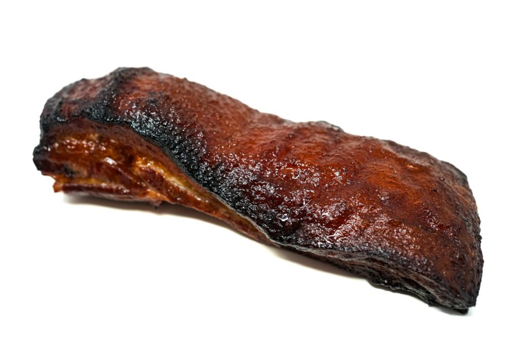 A slice of Momofuku-inspired pork belly with a mahogany-colored caramelized exterior, visible layers of tender meat and rendered fat, glistening with the sweet-savory glaze characteristic of the famous restaurant recipe.
