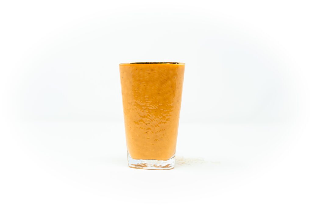 A creamy orange papaya coconut fig smoothie served in a clear glass, topped with shredded coconut on a white background.