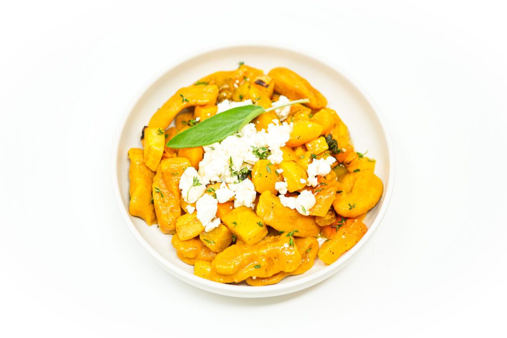 A bowl of Autumn Harvest Pumpkin Gnocchi, featuring tender gnocchi made from pumpkin puree, served with roasted yellow beets, rutabaga, and butternut squash, drizzled with a rich brown butter sage sauce and topped with crumbled goat cheese and fresh thyme.