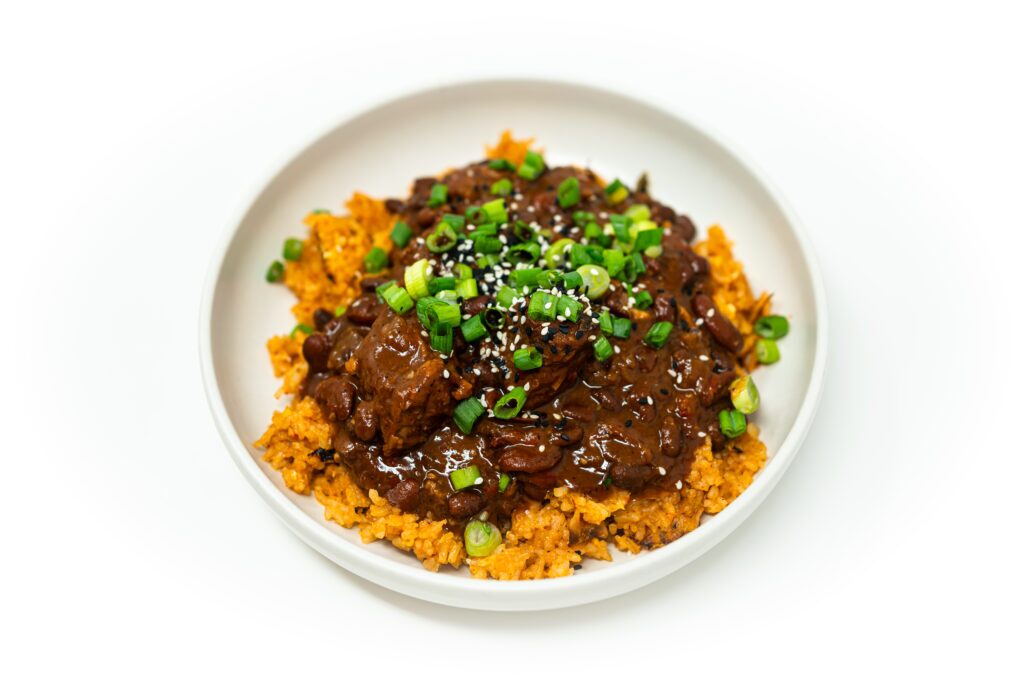 A bowl of Korean BBQ-inspired beef chili over kimchi fried rice, topped with green onions and a drizzle of sesame oil.