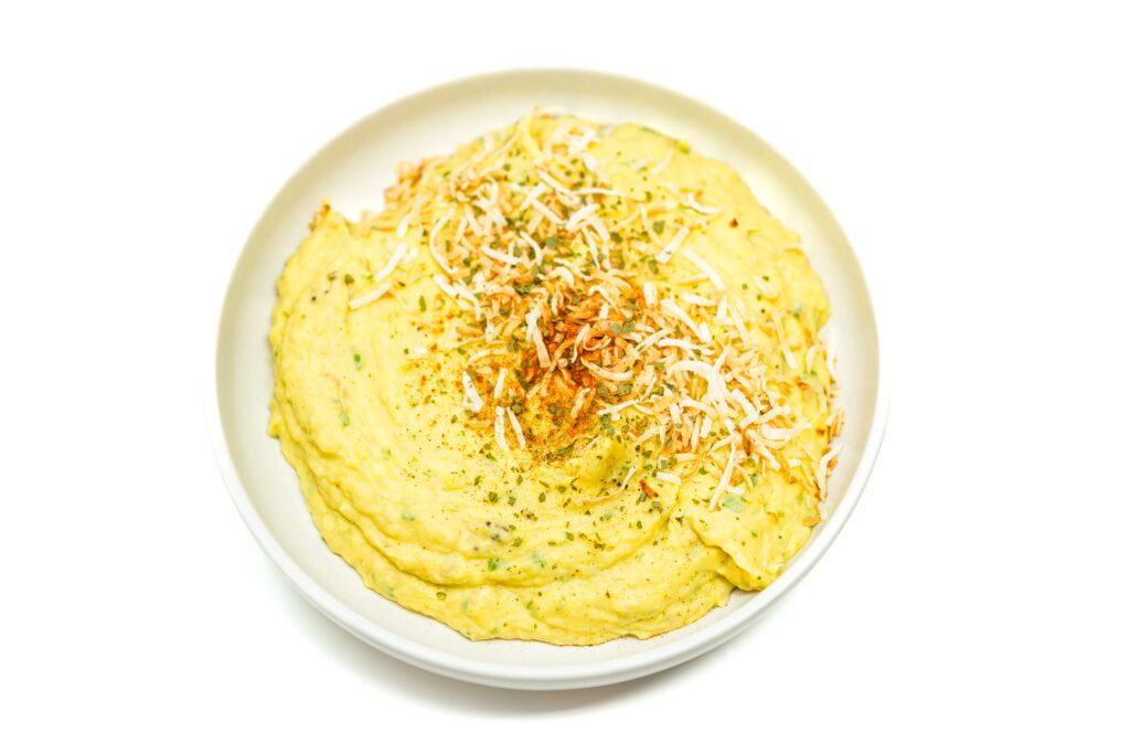 Mashed Caribbean Creamed Plantains garnished with chopped toasted coconut and paprika, showcasing the creamy texture of the plantains combined with vibrant green onions for a flavorful dish.
