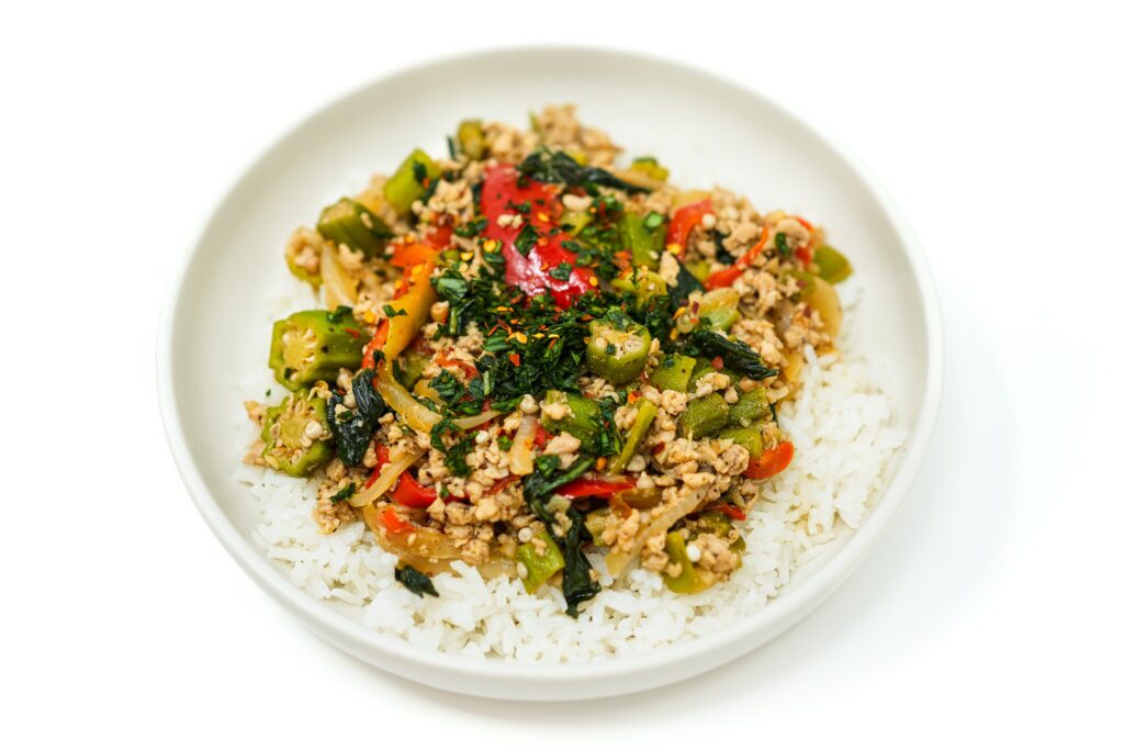 A colorful plate of Thai-Inspired Chicken, Okra, and Basil Stir-Fry featuring ground chicken, sliced red bell peppers, and fresh okra, garnished with vibrant basil leaves and served over a bed of jasmine rice.