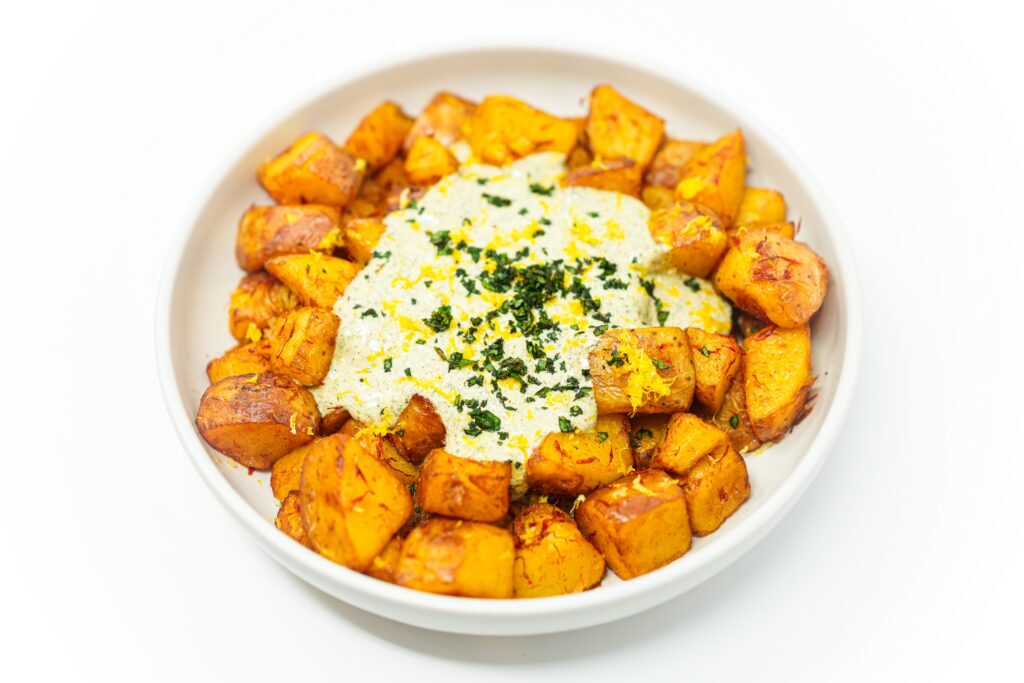 A bowl of golden saffron-roasted potatoes garnished with fresh parsley and lemon zest, served alongside a creamy yogurt za'atar dip.