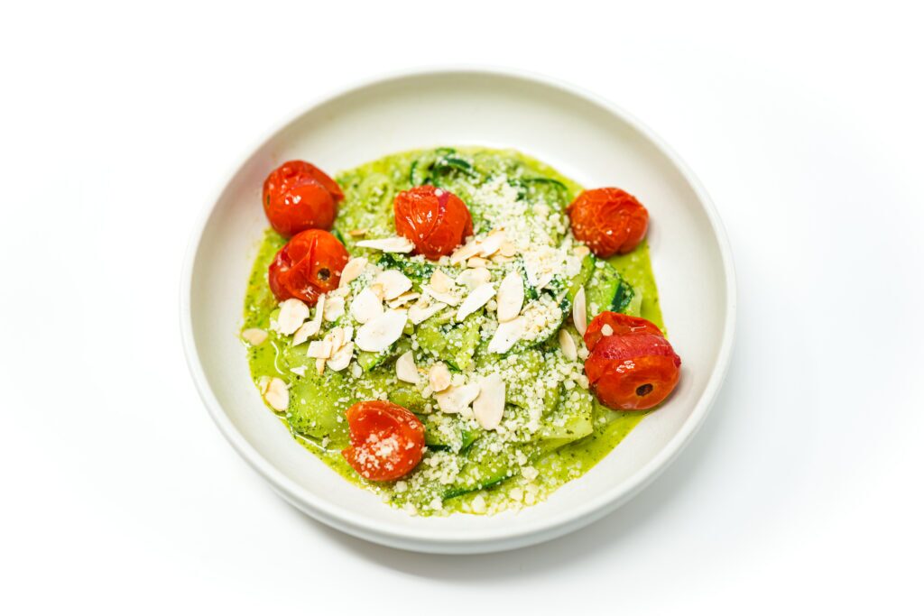 A vibrant plate of zucchini noodles tossed in creamy pesto, topped with roasted cherry tomatoes and garnished with toasted almond slices and Parmesan cheese