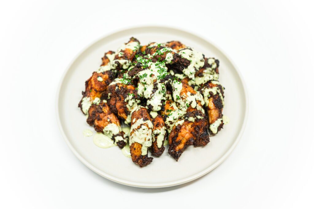 Golden brown slow-roasted chicken wings served with a side of creamy scallion ranch dip on a rustic plate, garnished with fresh herbs.