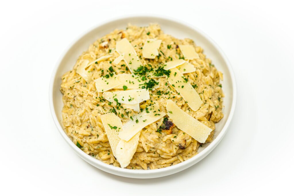 A bowl of roasted cauliflower Parmesan orzo featuring creamy orzo pasta mixed with caramelized cauliflower, topped with freshly grated Parmesan and chopped parsley.
