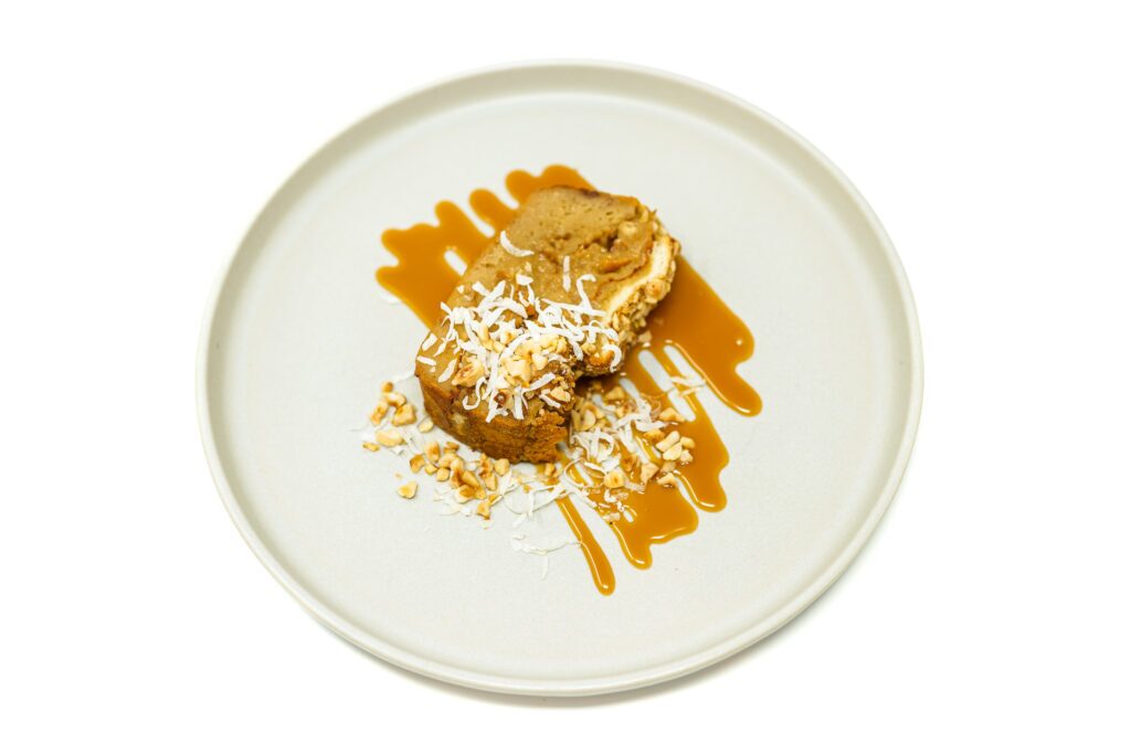 Hawaiian Roll Macadamia Nut Bread Pudding topped with coconut caramel sauce, served in slices with macadamia nuts and a drizzle of caramel.