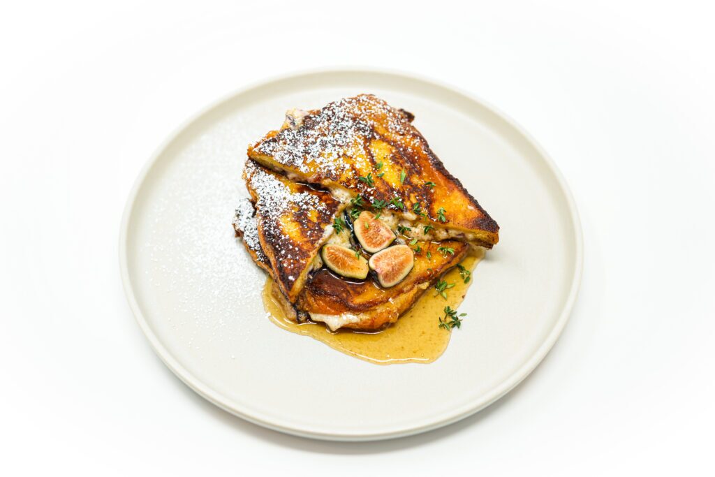 Golden brioche French toast stuffed with creamy mascarpone and fresh figs, drizzled with thyme-infused maple syrup and garnished with sliced figs.