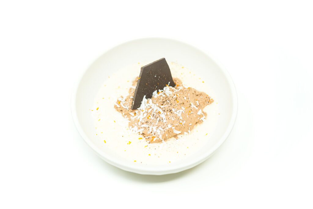 A dark chocolate mousse quenelle set over whipped coconut cream, topped with chili powder, toasted coconut flakes, and chocolate bark.