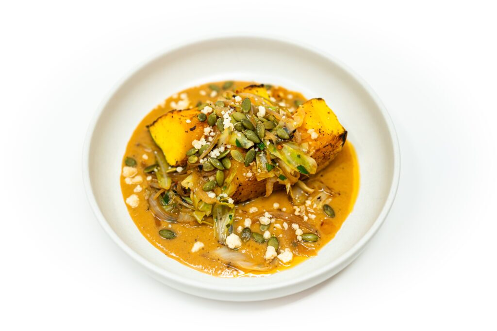 Seared pumpkin steak with miso brown butter sauce, charred cabbage, onion, chili oil, pepitas, and Parmesan on a plate