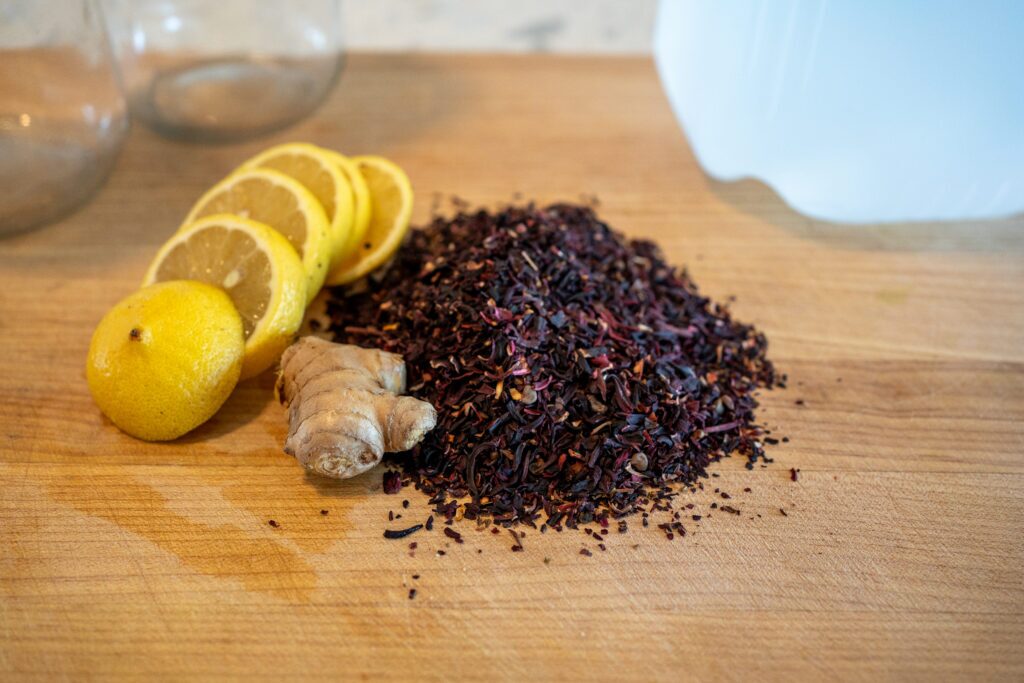 Hibiscus tea ingredients including dried hibiscus flowers, fresh ginger root, and lemons on wooden cutting board