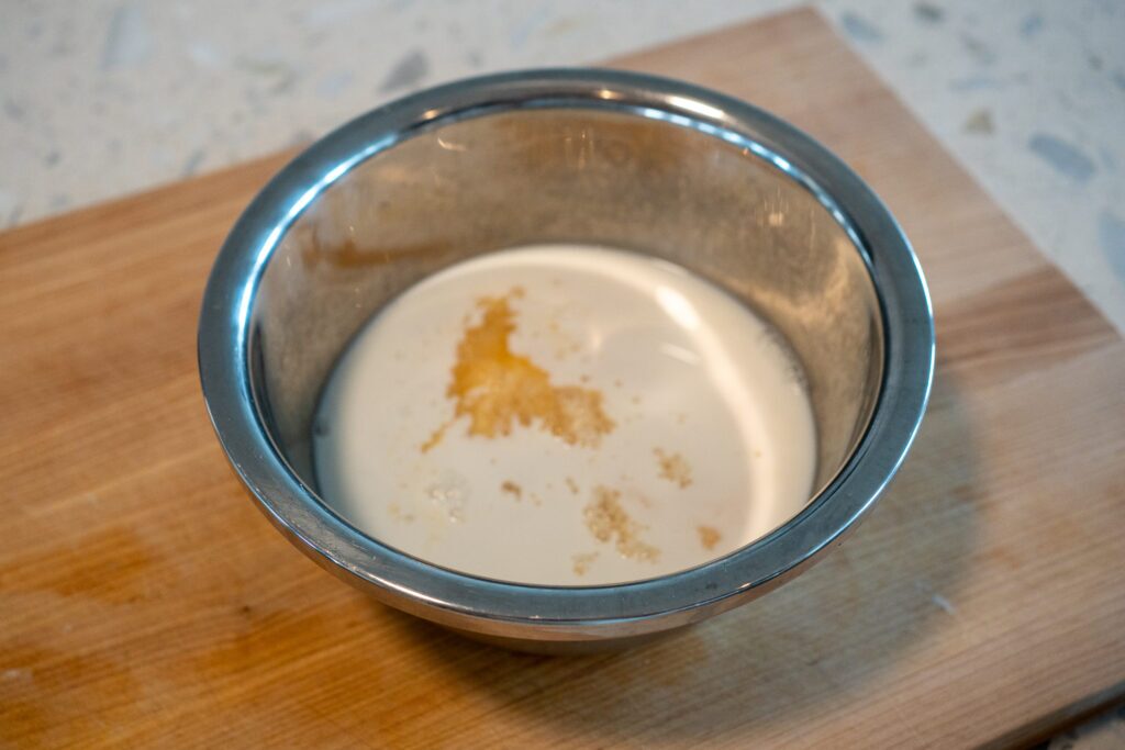 Milk washing persimmon purée in a stainless steel mixing bowl, showing visible milk curds separating from the fruit mixture.