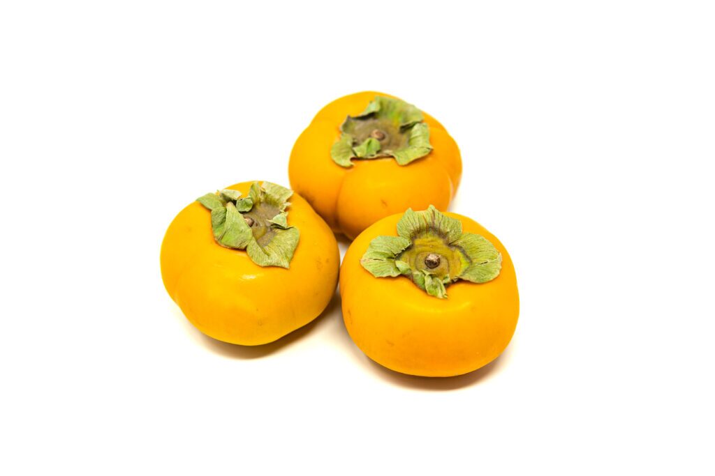 Three ripe Fuyu persimmons with green tops intact on a white background.