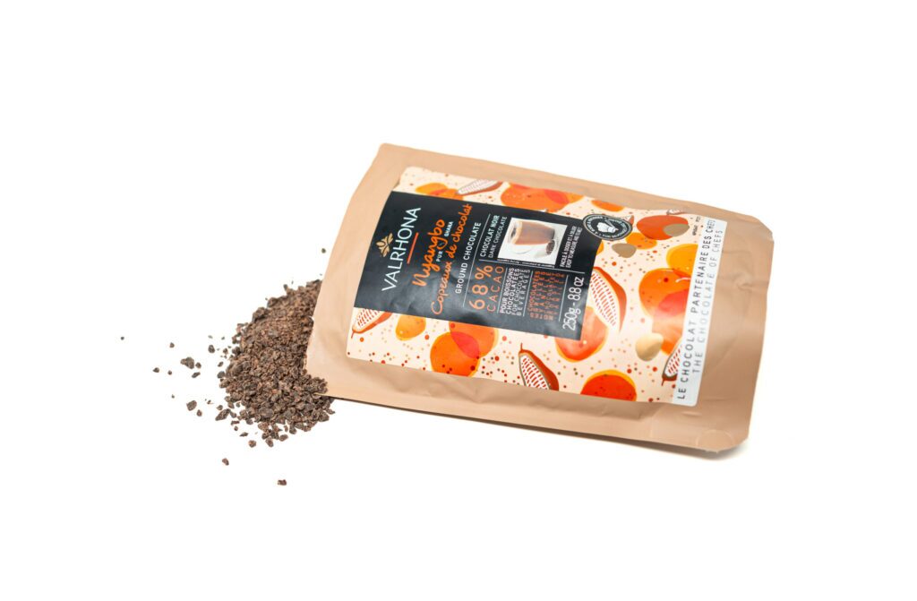 A bag of Valrhona Nyangbo 68% single origin ground dark chocolate lying flat on a white surface, with rich chocolate shavings spilling out from the opening.