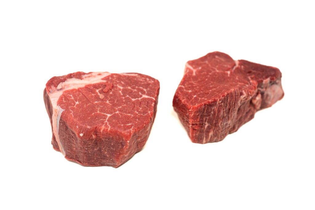 Two raw filet mignon steaks on a white background, one in the foreground and one slightly behind.