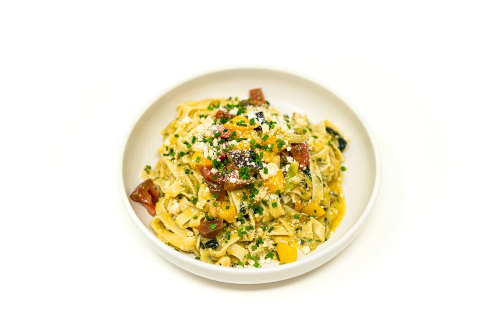 A bowl of zucchini butter noodles topped with marinated heirloom tomatoes, fresh chives, and grated parmesan cheese.