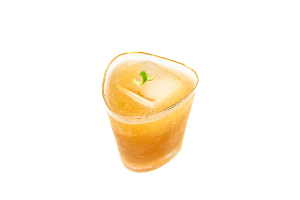 A chilled rocks glass filled with a dark amber Tamarind Agave Batanga, garnished with a lime wheel, sitting next to a bottle of Tamarind Jarritos.
