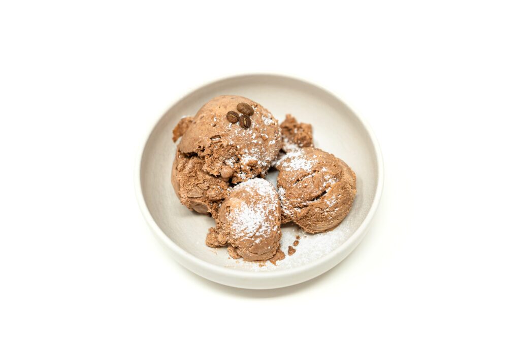 Three scoops of dark coffee, cocoa, and agave ice cream in a ceramic bowl, dusted with powdered sugar and topped with whole roasted coffee beans.