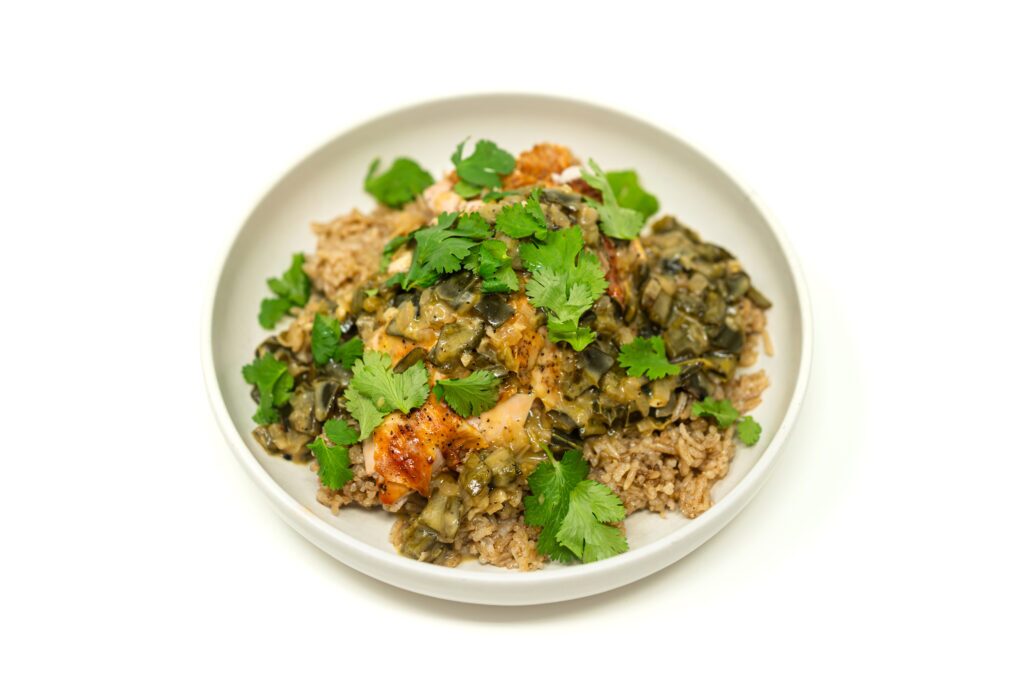 Sliced, cast-iron seared chicken breast resting on brown rice, smothered in a thick, brick-red spiced poblano cream sauce and topped with fresh cilantro.