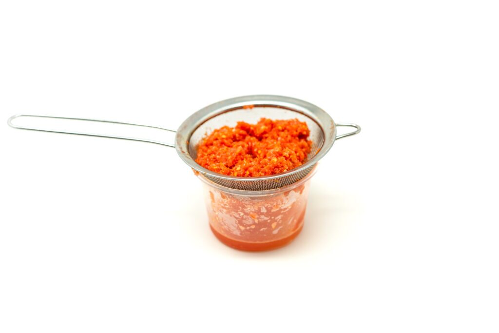 Straining lacto-fermented tomatoes through a fine-mesh sieve to separate the clear, acidic tomato water from the dense, umami-rich pulp.