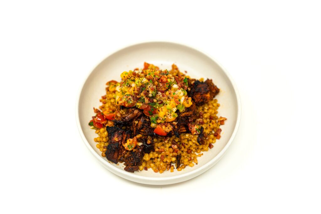 A warm bowl of crisped carnitas-style Texas pork ribs piled over pancetta pearl couscous and topped with bright cherry tomato salsa.