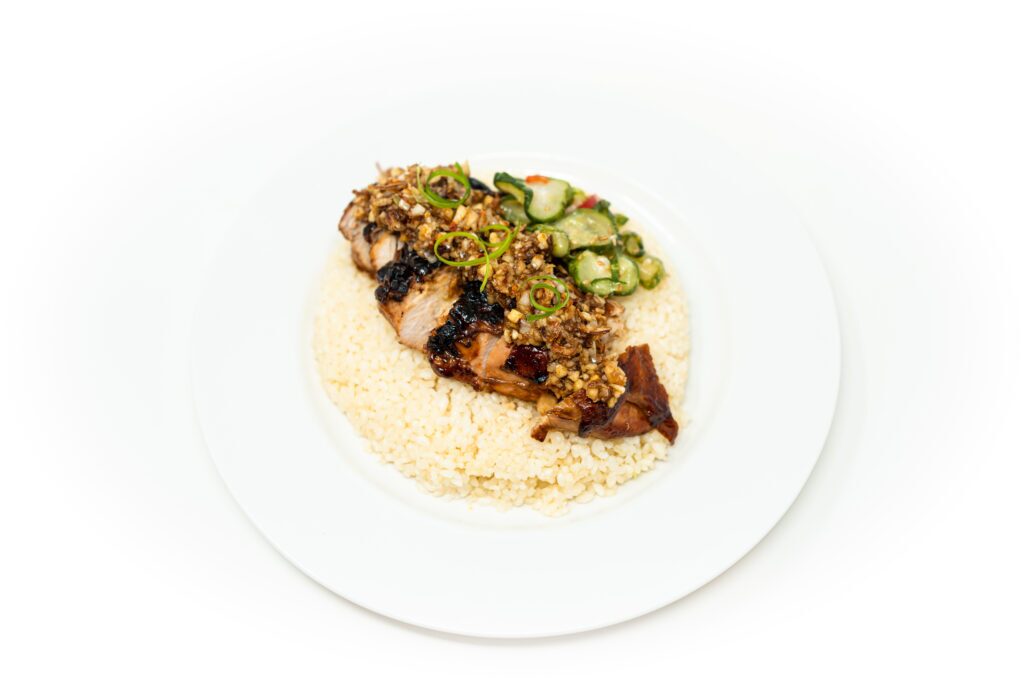 Sliced skin-on chicken breast lacquered with a dark charred glaze resting on a bed of white rice with ginger scallion oil.